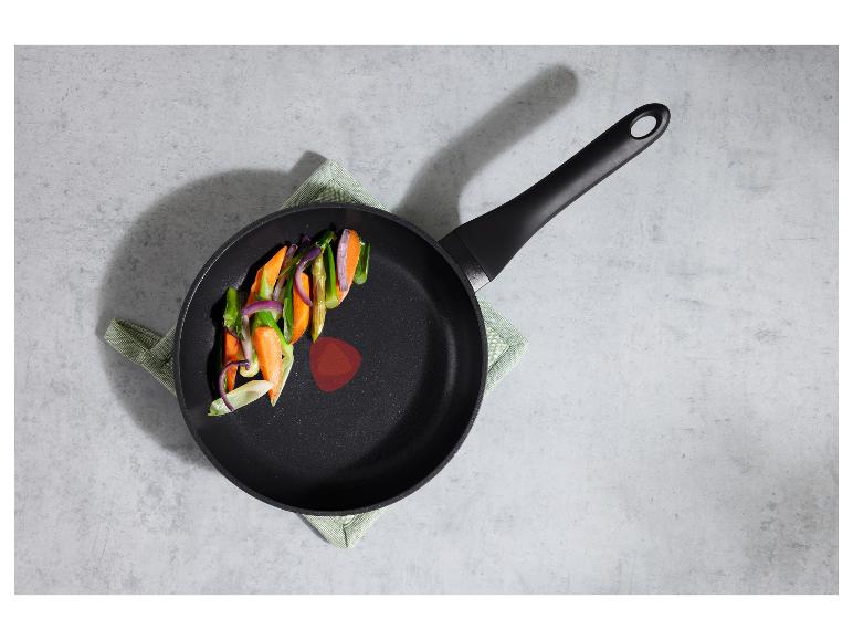 Koekenpan met groenten op een grijze ondergrond met een groene doek.