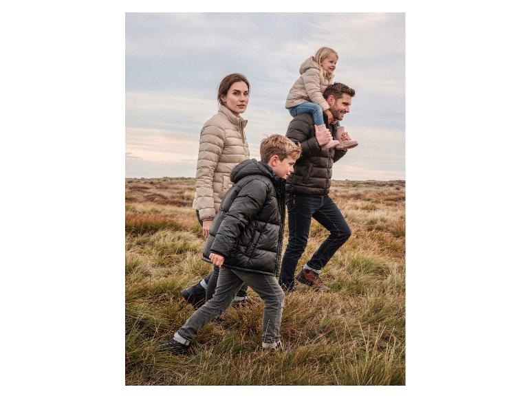 Familie in warme jassen en stevige schoenen wandelt door een graslandschap.