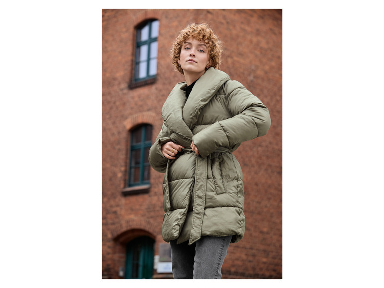 Een vrouw in een groene gewatteerde jas met een riem.