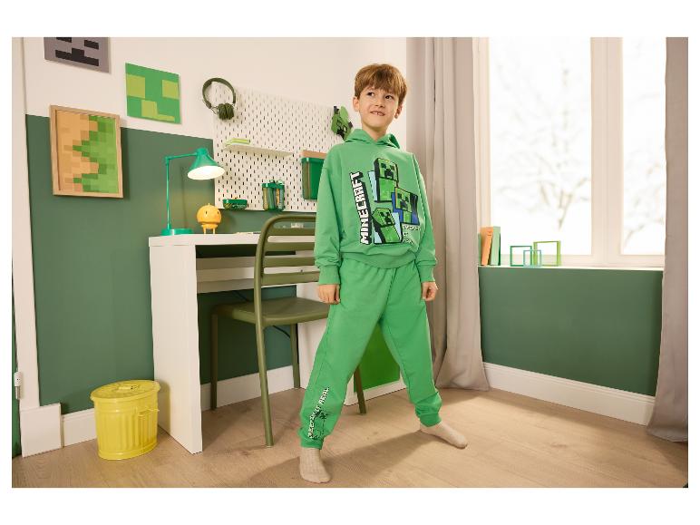 Jongen in groen Minecraft-trainingspak in een kamer met themadecoratie.