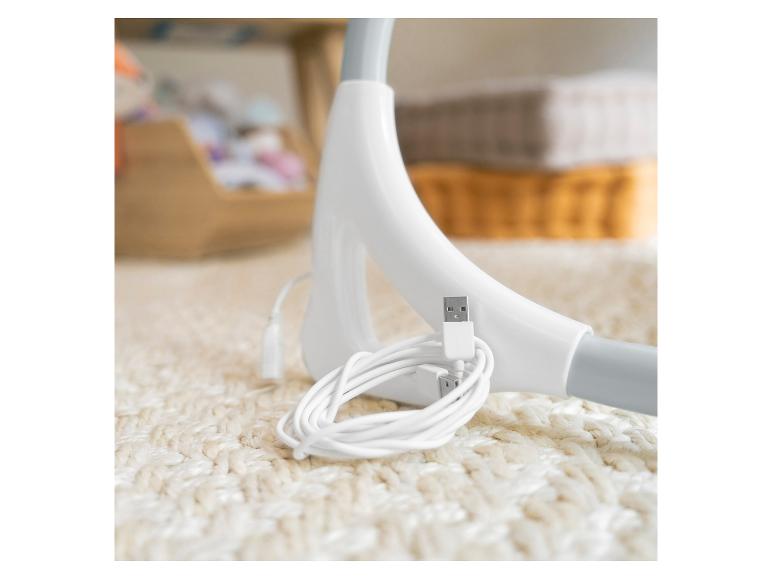 Witte USB-kabel en oplader op een wit tapijt, met wazige voorwerpen op de achtergrond.
