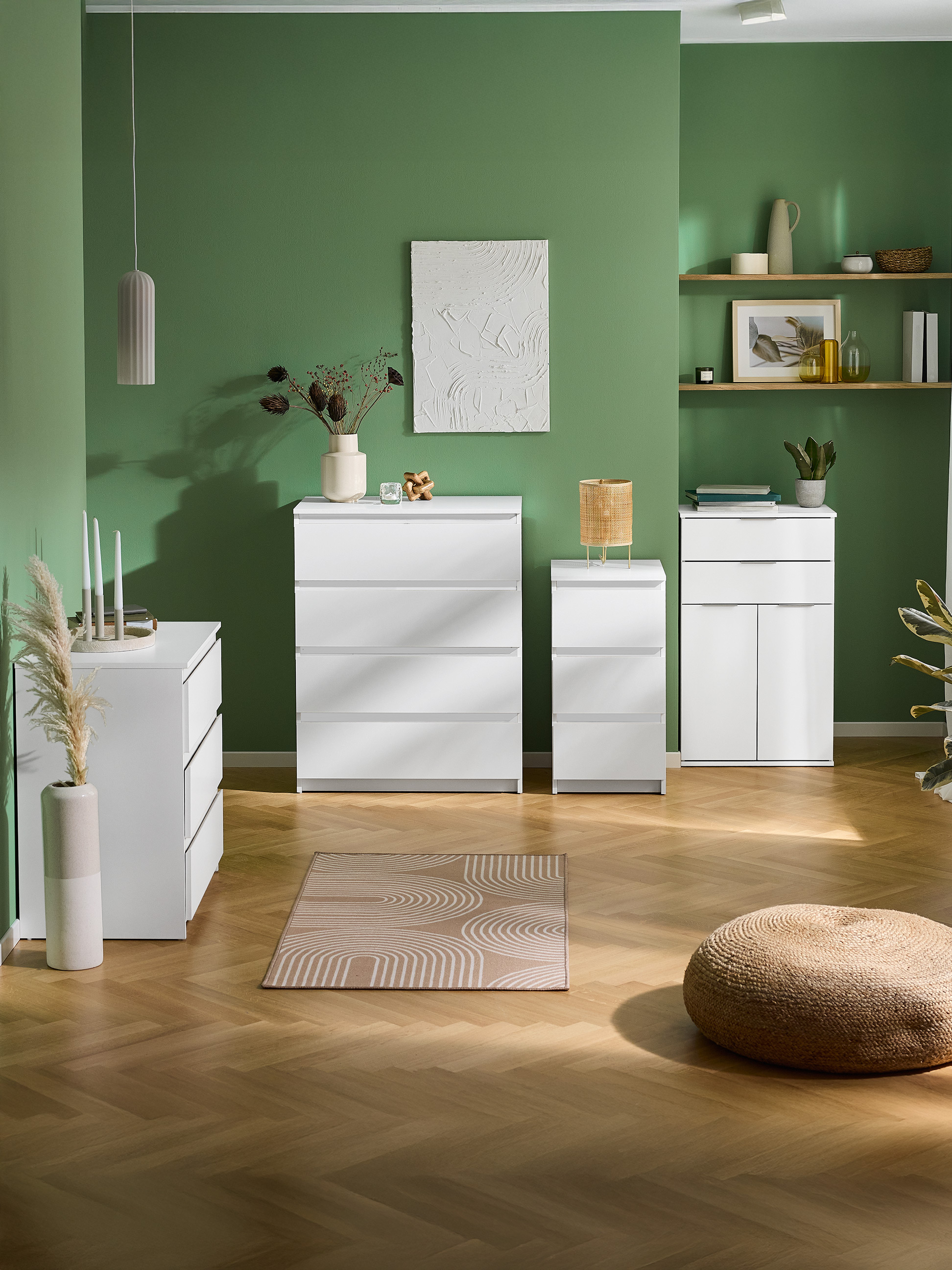 Witte ladekasten en kasten in een groene kamer met houten vloer en vloerkleed.