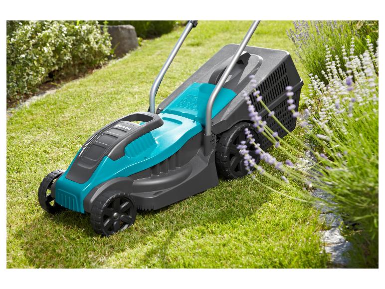 Grasmaaier op groen gras naast lavendelbloemen en een struik