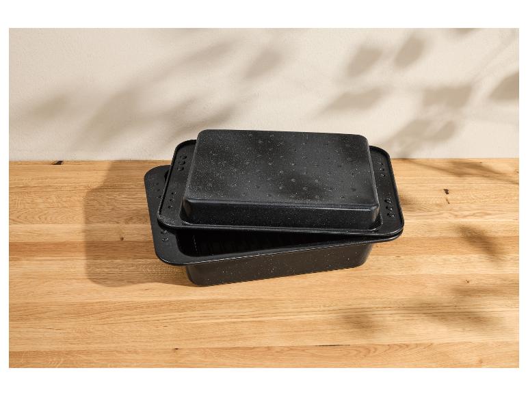 Twee zwarte rechthoekige braadsledes met gespikkeld oppervlak op een houten ondergrond.