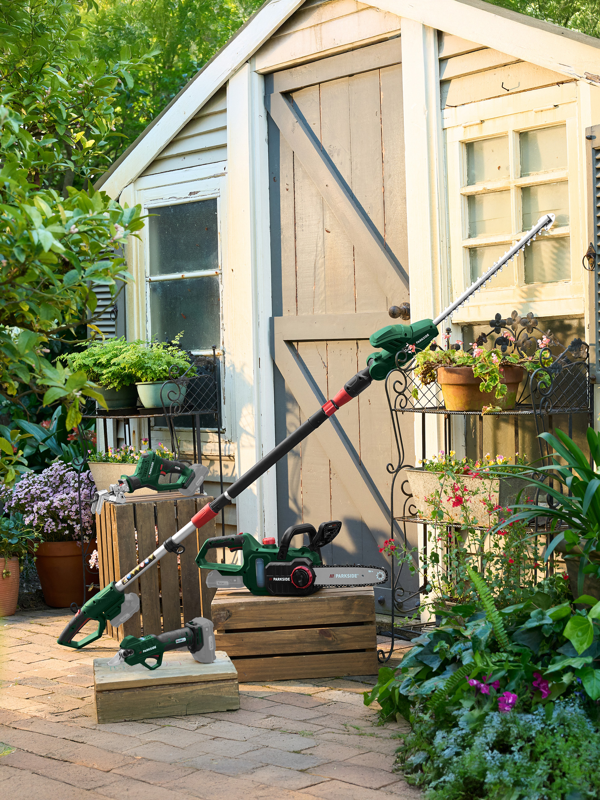 Parkside tuingereedschap: telescopische heggenschaar, kettingzaag en snoeischaar in een tuinsetting.