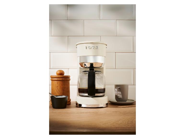 Een crèmekleurige koffiezetapparaat 1973 op een houten tafel.