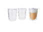 Drie dubbelwandige glazen, twee leeg en één met een latte macchiato.