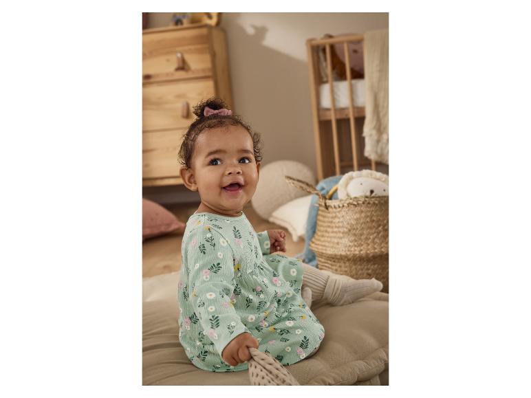 Blauwe baby in bloemenjurk zit op een kussen in een kinderkamer.