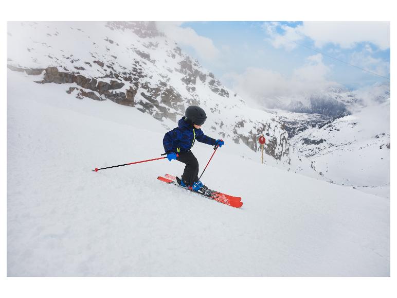 Kind in blauwe ski-uitrusting en zwarte helm skiet van een besneeuwde berghelling.