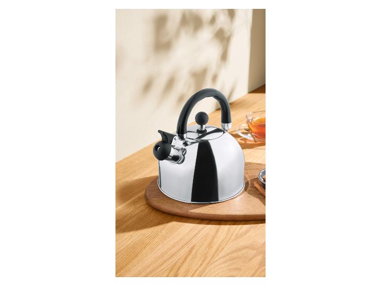 Glanzende metalen theeketel met zwart handvat op een houten tafel met een kopje thee.