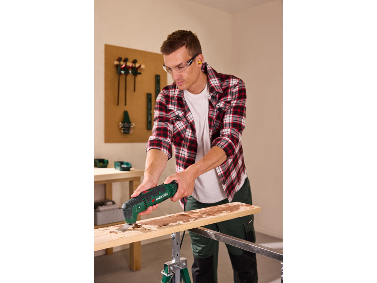 Man gebruikt een multitool om hout te schrapen, draagt veiligheidsbril en oordopjes.
