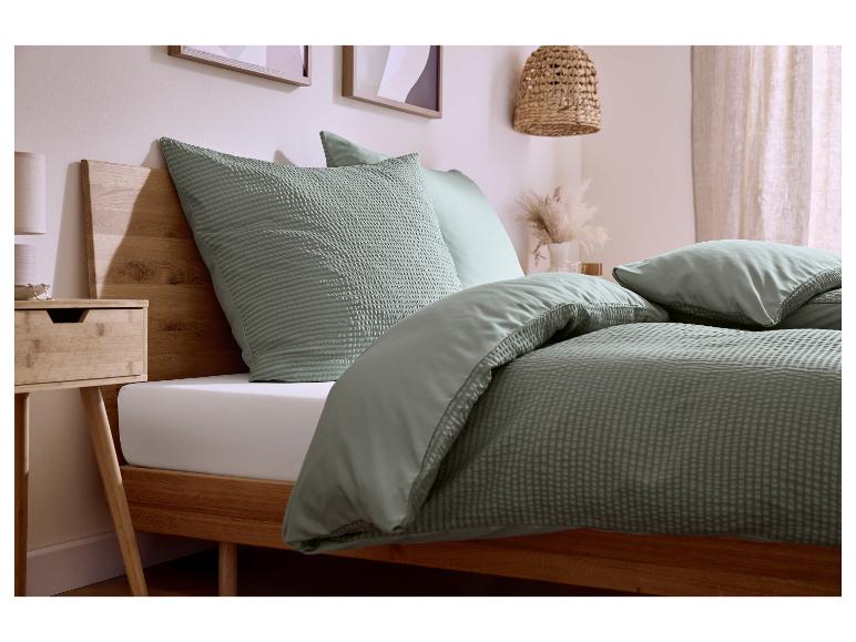 Slaapkamer met houten bedframe, saliegroen wafeldekbedovertrek en kussens.