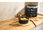 Een zwarte siliconen airfryer-mand gevuld met kreukelfrietjes op een houten plank naast een airfryer