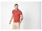 Man in een rood poloshirt met logo, beige korte broek en armbanden, kijkt naar rechts.