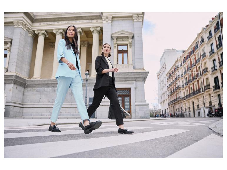 Twee vrouwen in elegante pakken steken een zebrapad over.