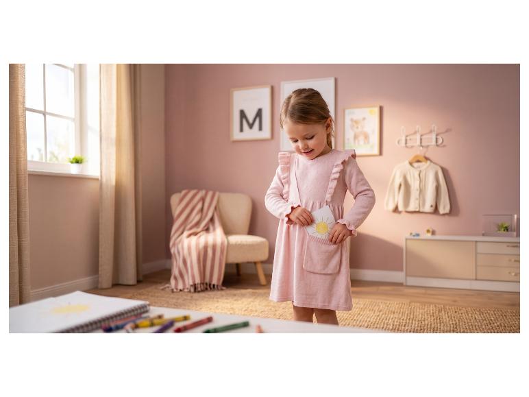 Meisje in roze jurk stopt zonnetekening in zak, in een kinderkamer.