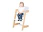 Lachend klein meisje zit in een houten en witte kinderstoel.