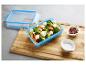 Blauwe voedselcontainer met broccoli- en zoete aardappelsalade met fetakaas, zout en peper.