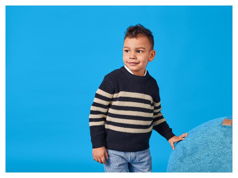 Een lachende jongen in een gestreepte trui, leunend op een groot kussen.