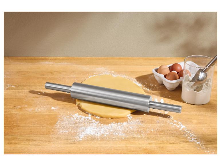 Roestvrijstalen deegroller met deeg, bloem en eieren op een houten aanrecht.