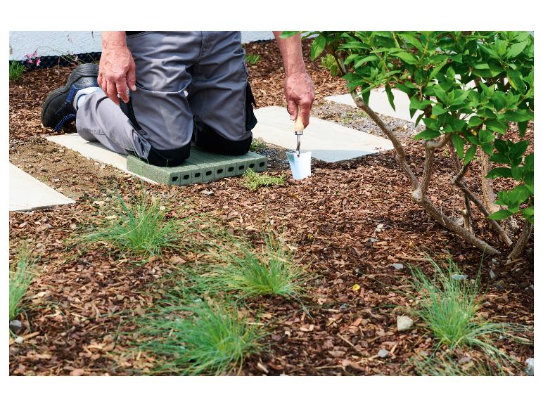Man knielt op tuinkussen, plant met een handschepje.
