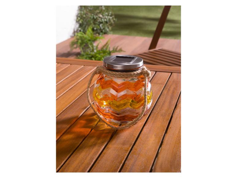 Een gele, oranje en witte glazen zonnelamp met touwhandgreep op een houten tafel.