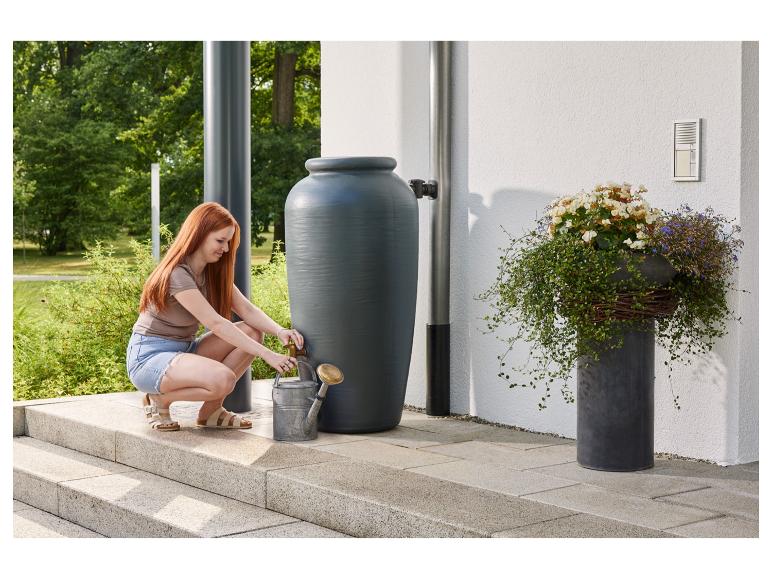 Vrouw vult gieter uit regenton in de tuin.