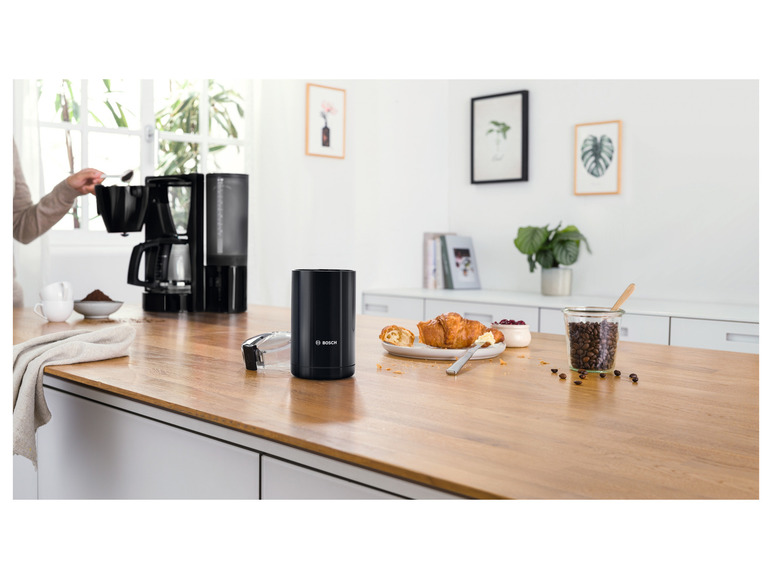 Een zwarte Bosch koffiemachine en een pot koffiebonen op een houten aanrecht.