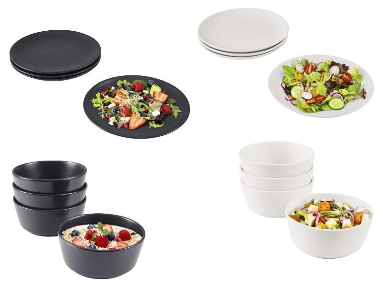 Zwarte en witte keramische borden en kommen met salades en havermout met bessen.