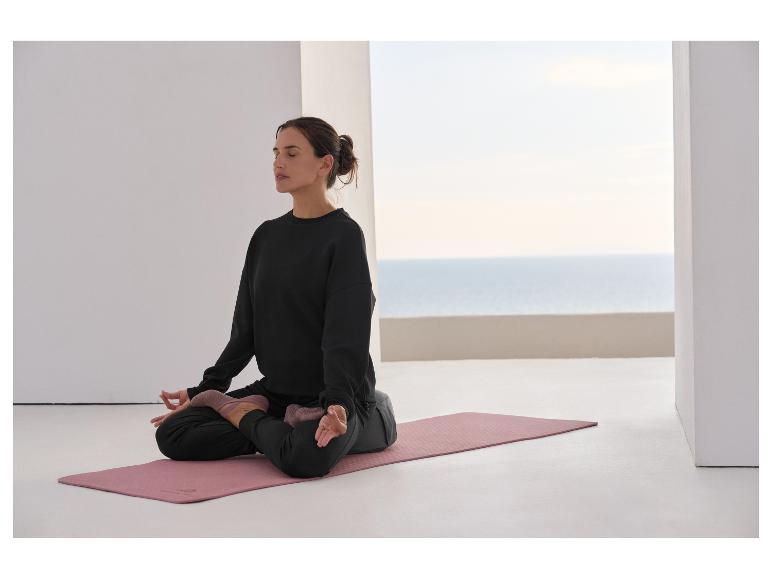 Vrouw mediteert op een yogamat, draagt een zwart sweatshirt en broek.