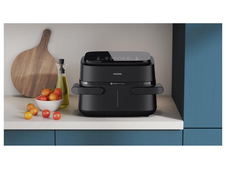 Een zwarte Philips airfryer op een aanrecht met tomaten en olijfolie.