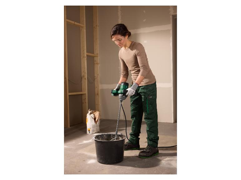 Vrouw mengt mortel in een emmer met een elektrische mixer, draagt veiligheidsbril en handschoenen.
