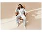 Vrouw in een comfortabele witte loungewear set, zittend in een bruine fauteuil met raamlicht.