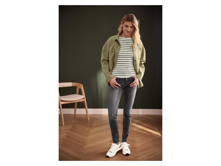 Vrouw draagt groene jas, gestreepte top, grijze jeans en witte sneakers.