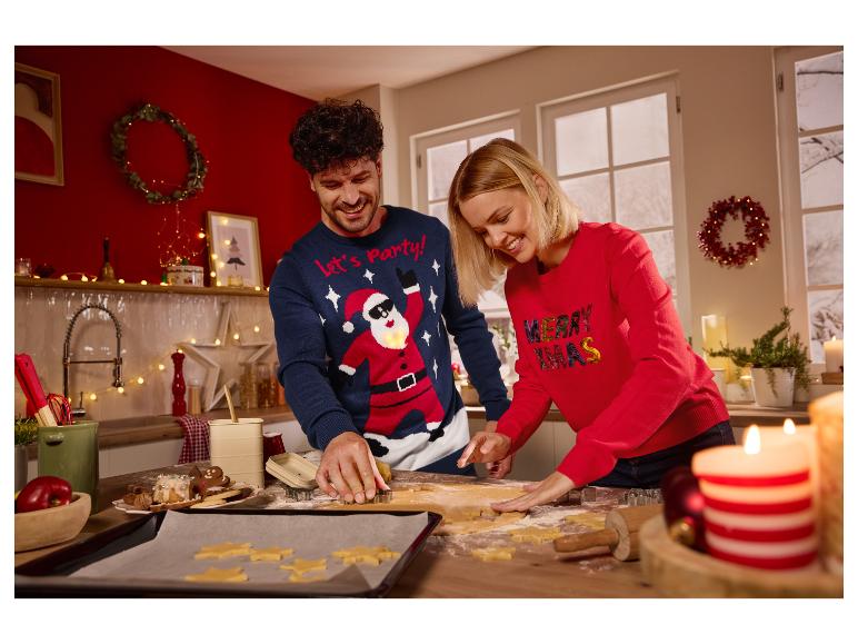 Een lachend stel draagt kersttruien en snijdt koekjes in de keuken.