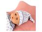 Babypop in een wit slaappakje en muts met bosdierenprint, liggend op een roze kussen.