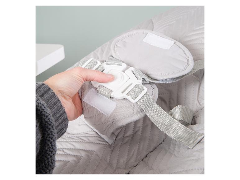 Hand die de gesp van een grijs gewatteerd babyzitje of wipstoeltje vastmaakt.