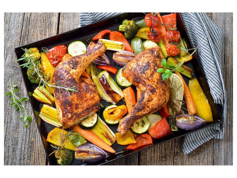 Geroosterde kipdrumsticks met groenten zoals paprika, courgette en uien op een bakplaat.