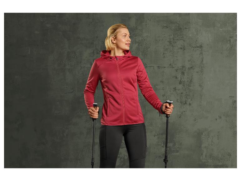 Vrouw in een rode jas en zwarte broek met wandelstokken.