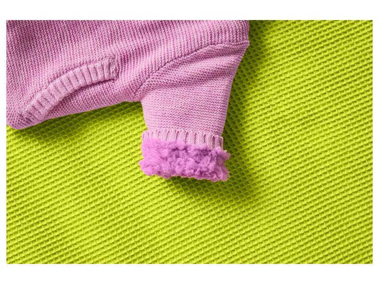 Roze gebreide mouw met een pluizige manchet op een getextureerde groene stof