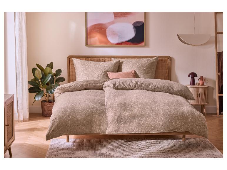 Slaapkamer met houten bed, beige beddengoed met patroon en een plant.