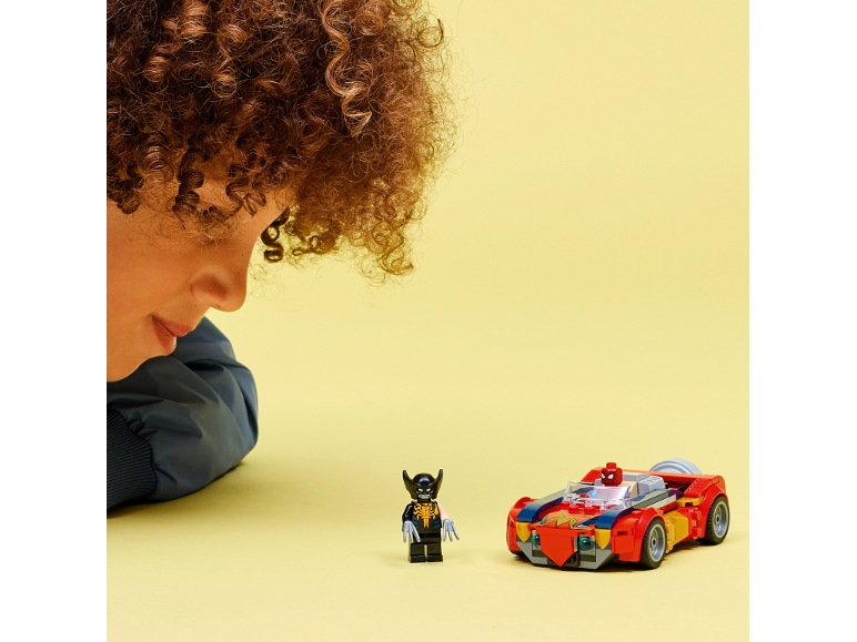 Een kind kijkt naar een speelgoedsuperheld en een rode speelgoedauto op een gele achtergrond.