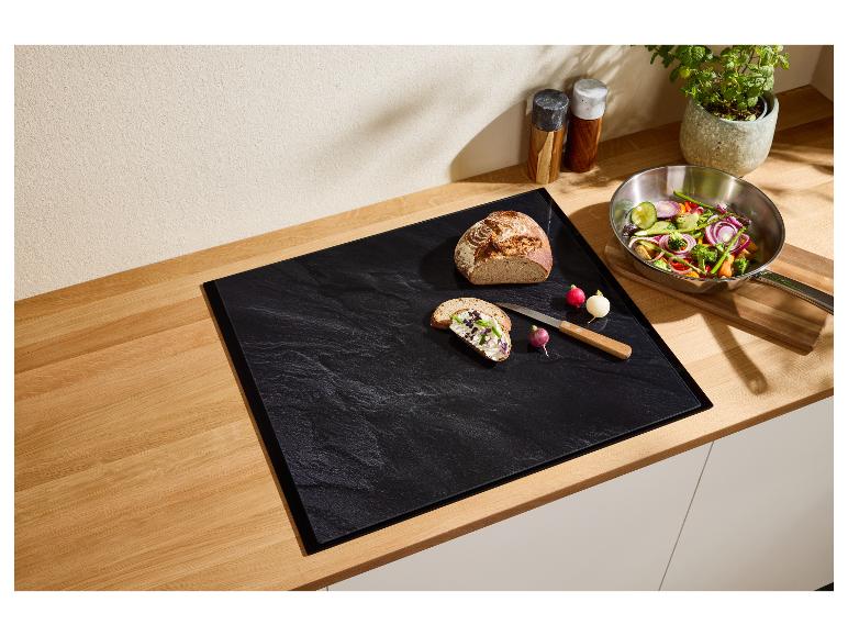 Aanrecht met zwarte snijplank, brood, radijsjes en een pan met groenten.