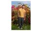 Man in geel T-shirt en donkergroene broek poseert voor bloemen.