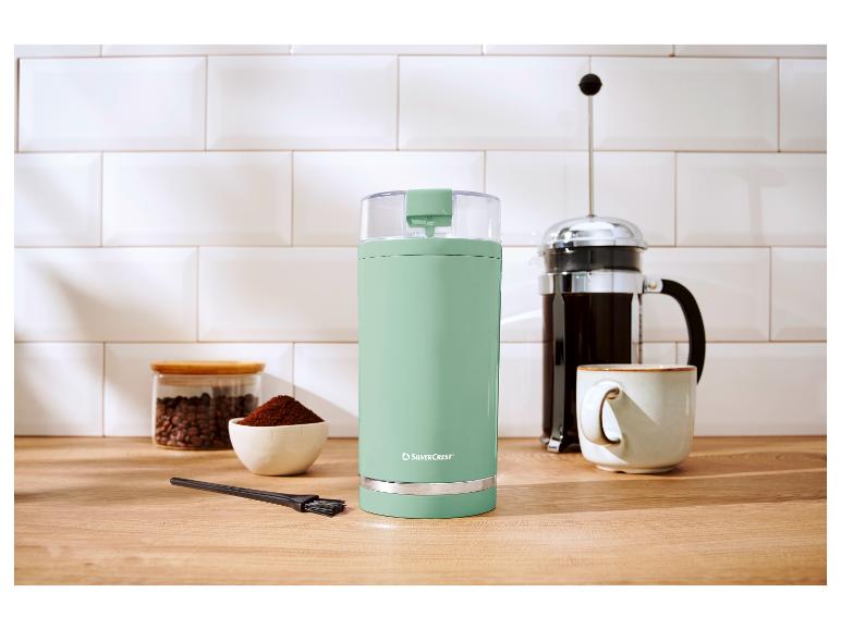 Mintgroene SilverCrest koffiemolen op een houten aanrecht met een french press en mok.