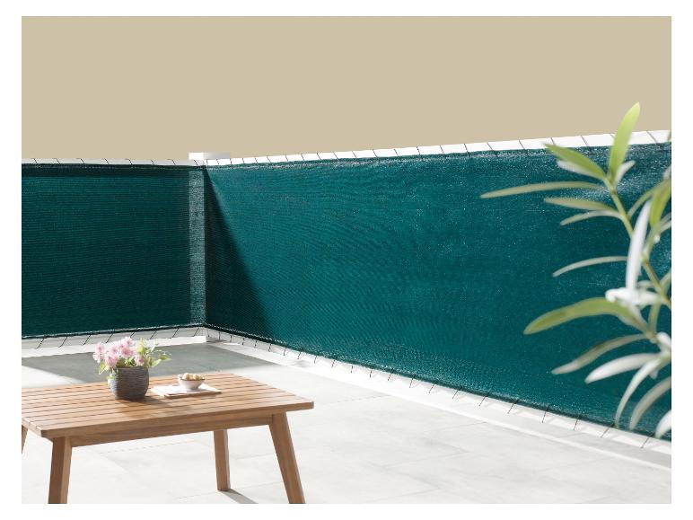 Donkergroen balkon privacyscherm, met een houten tafel en potbloemen.