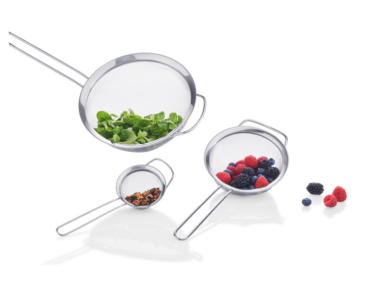 Drie metalen zeefjes met handvatten, gevuld met sla, bessen en thee.