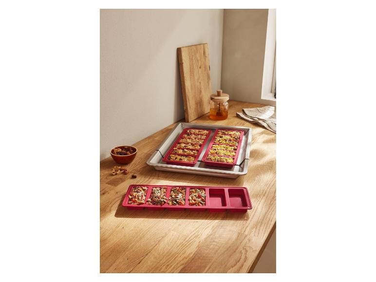 Rode siliconen bakvormen voor granola repen op een houten oppervlak.