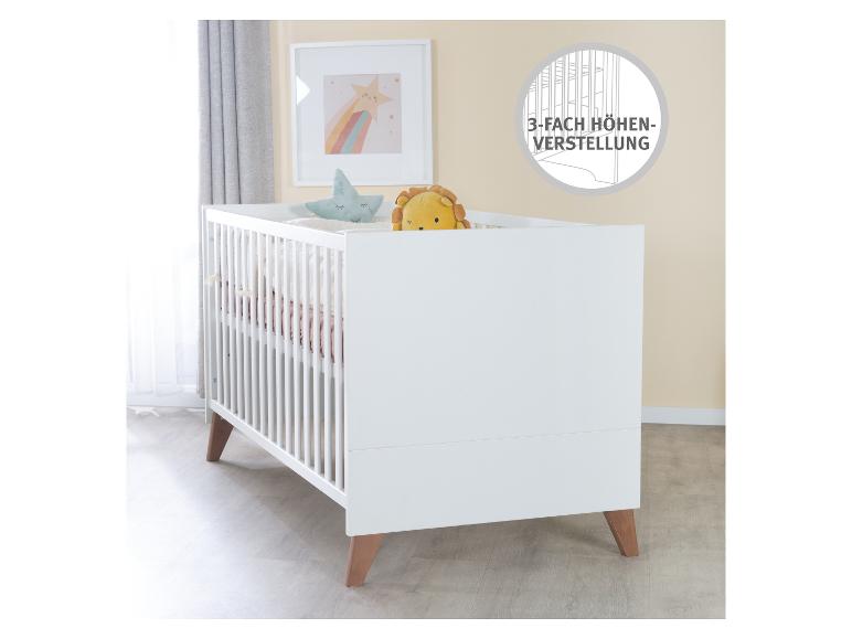 Wit babybedje met houten poten, met een leeuwenspeeltje en een sterrenkussen.