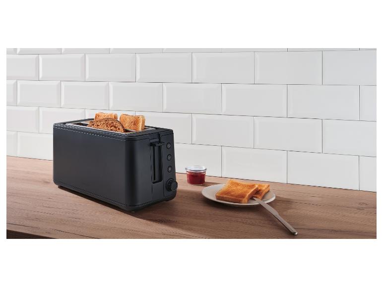 Zwarte broodrooster met toast, jam en botermes op een houten aanrecht voor witte tegels.